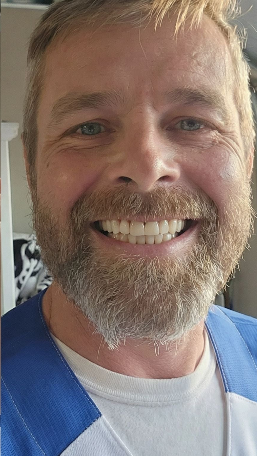 Man with a beard and mustache smiling, wearing a blue and white shirt.