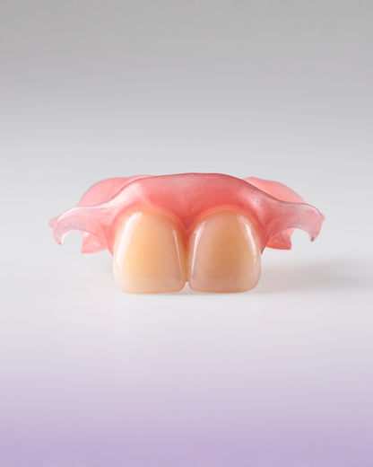A dental appliance showing two artificial front teeth set in a pink gum-like base, photographed on a clean light gray to white studio background.