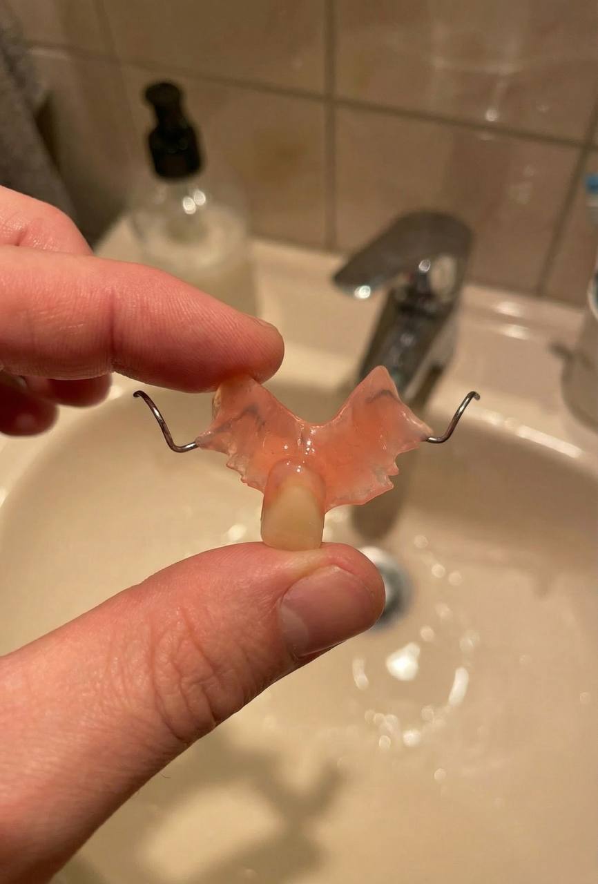 Hand holding a dental flipper over a bathroom sink with a faucet in the background