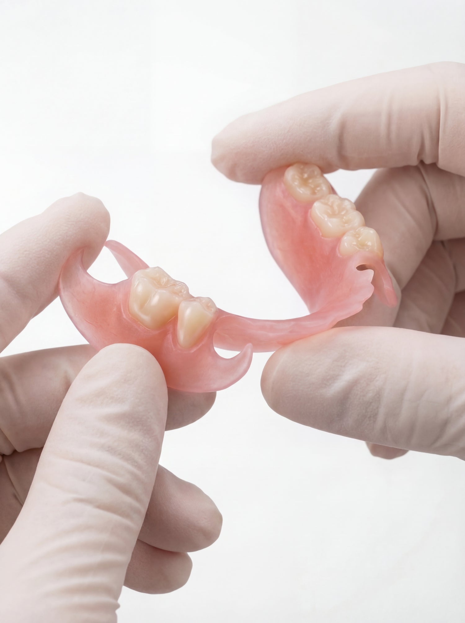 Flexible Partial denture for missing back teeth on white background held with fingers in gloves