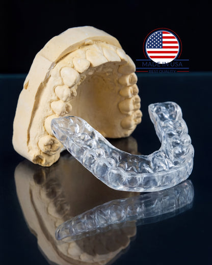 Clear dental aligner on a model of teeth with a USA flag logo in the corner.
